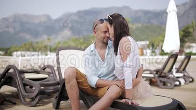 我爱坐在躺椅上的这对夫妇，他们在海边和山的背景下互相陪伴